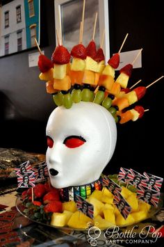 a white mask with fruit on it and sticks sticking out of the face to eat