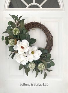 a wreath with white flowers and greenery is hanging on the front door, next to a window