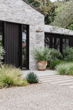 a stone house with black doors and plants in the front yard, along with gravel steps leading up to it