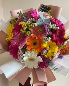 a bouquet of colorful flowers is wrapped in pink and white paper with a name tag on it