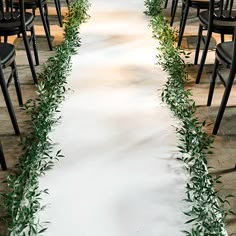 the aisle is lined with black chairs and greenery on each side, along with a white runner