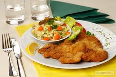 a white plate topped with fried chicken next to a bowl of salad and a fork