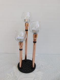 three glass candlesticks are sitting on a black stand with a white lace tablecloth