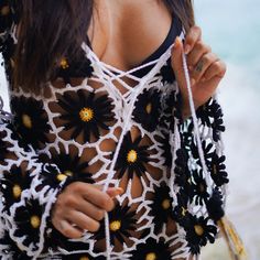 a woman wearing a crochet top with flowers on the front and back, holding a string