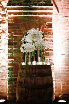 white flowers in vases sitting on top of a barrel next to a brick wall