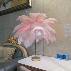 a pink feather lamp sitting on top of a table next to a chair and clock