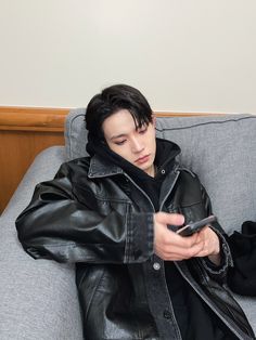 a man sitting on a couch looking at his cell phone while wearing a leather jacket