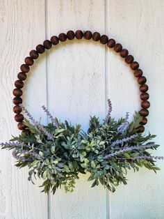 a wooden beaded wreath with greenery hanging on the side of a white wall