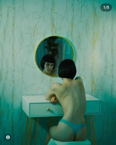 a naked man sitting in front of a mirror on top of a table next to a dresser