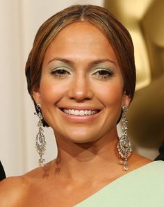 a smiling woman in a green dress with large earrings on her head and an oscar statue behind her