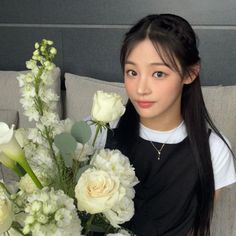 a woman sitting on a couch next to a bouquet of white flowers and greenery