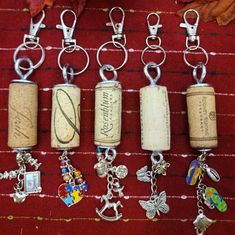 six wine cork keychains with charms attached to them on a red tablecloth