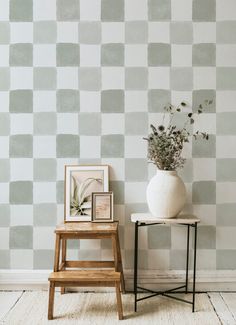 a white vase sitting on top of a wooden table next to a wall covered in squares