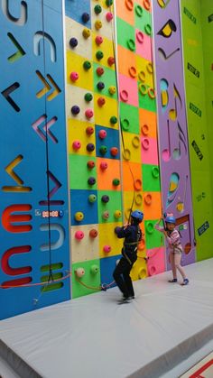 two children are climbing on the wall with colorful walls in the background and one child is holding onto a rope