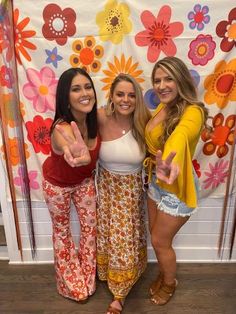 three beautiful women standing next to each other in front of a floral wallpapered backdrop