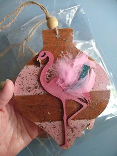 a pink flamingo ornament hanging from a string on a piece of wood