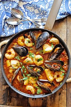 a pan filled with seafood and clams on top of a wooden table next to silverware