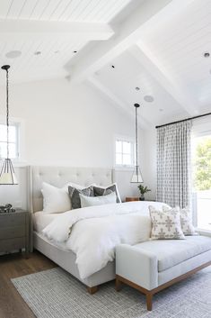 a bedroom with white bedding and pillows on top of the bedspread in front of two windows