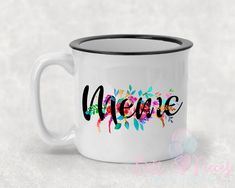 a white coffee mug with the word meme painted on it's side and colorful flowers