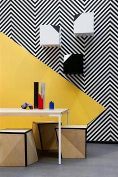 a table and two stools in front of a wall with black and white designs