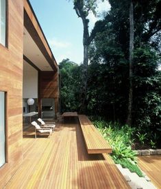 a wooden deck with lounge chairs and trees in the backgroung, next to an outdoor living area