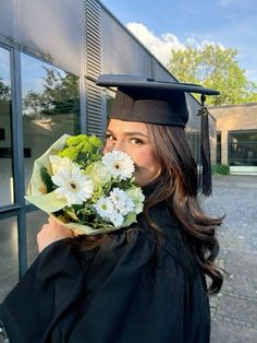 a woman wearing a graduation cap and gown holding flowers