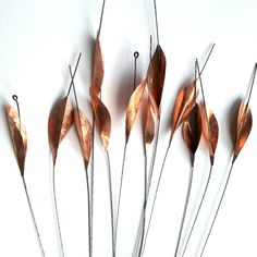 four metal stems with leaves attached to them on a white surface, in front of a white background