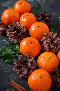 an arrangement of oranges and pine cones on a black surface with leaves, cinnamon sticks