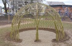 a circular structure made out of sticks in the middle of a park with children's play equipment behind it