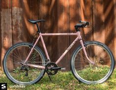 a pink bike parked in front of a wooden fence with grass on the ground next to it