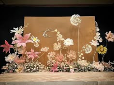 an arrangement of flowers on display in front of a brown backdrop with the letter d