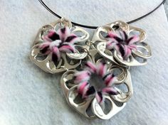 a close up of a necklace on a white surface with pink and black flowers in the center