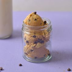 a glass jar filled with cookies and chocolate chips next to a bottle of milk on a purple surface