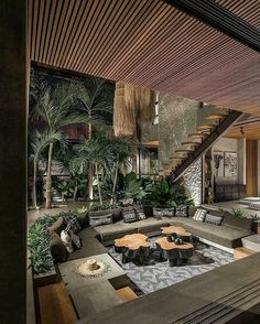 a living room filled with lots of furniture next to a stair case covered in plants