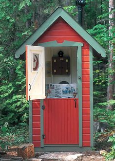 a small red shed in the woods with its door open and newspaper on it's side