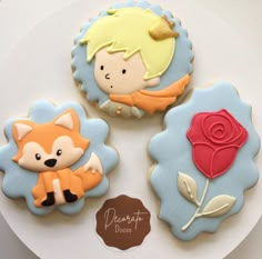 three decorated cookies sitting on top of a white cake plate next to a red rose