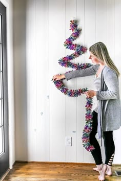 a woman standing in front of a christmas tree made out of tinsel and yarn