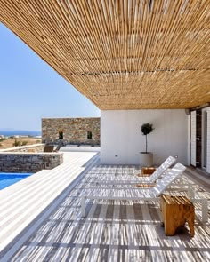 an outdoor covered patio with chaise lounges next to a swimming pool and stone walls