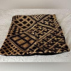 a black and gold blanket sitting on top of a white bed next to a pillow