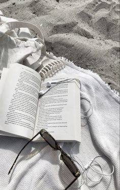 an open book sitting on top of a beach towel next to sunglasses and headphones