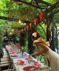 a woman in white dress standing over a table with red plates and napkins on it