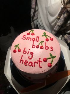 a pink cake with writing on it sitting in a white box next to a woman