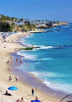 many people are on the beach with blue umbrellas in the sand and clear water