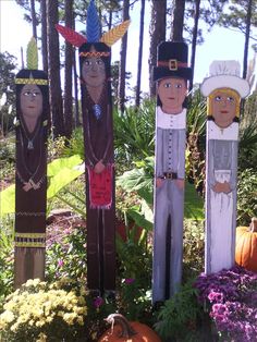 three scarecrows are standing next to each other in front of flowers and trees