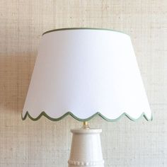 a white table lamp with a green trim on it's base, against a beige wall