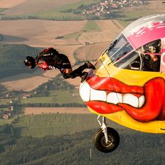 a man is hanging from the side of an airplane with a mouth painted on it