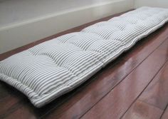 a white and black striped mattress on the floor in front of a window with no curtains