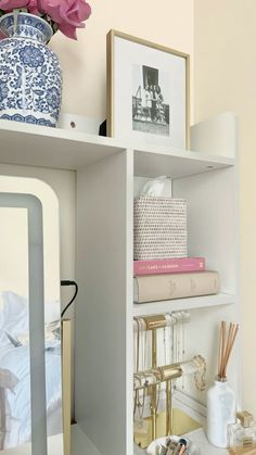 a white shelf filled with lots of books and other items next to a vase on top of a table