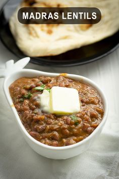 a white bowl filled with food next to a pita bread on top of a table