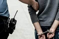 two people are holding hands with handcuffs on their wrists, and one person is wearing a police uniform